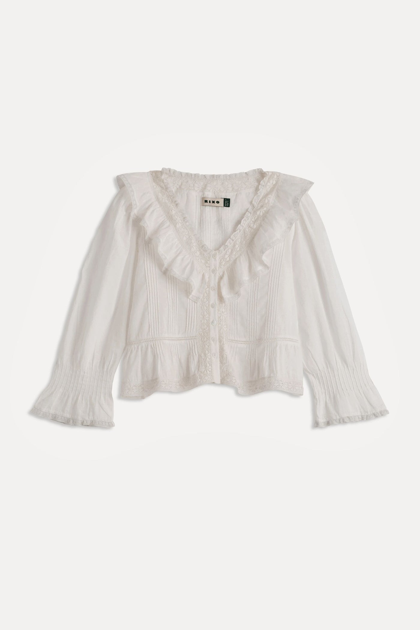 The Solene - Ivory is a white, long-sleeved blouse featuring a ruffled V-neckline, vintage-style pintuck detailing, flared textured cuffs, and a delicate feminine touch—perfect for fans of vintage-inspired fashion.
