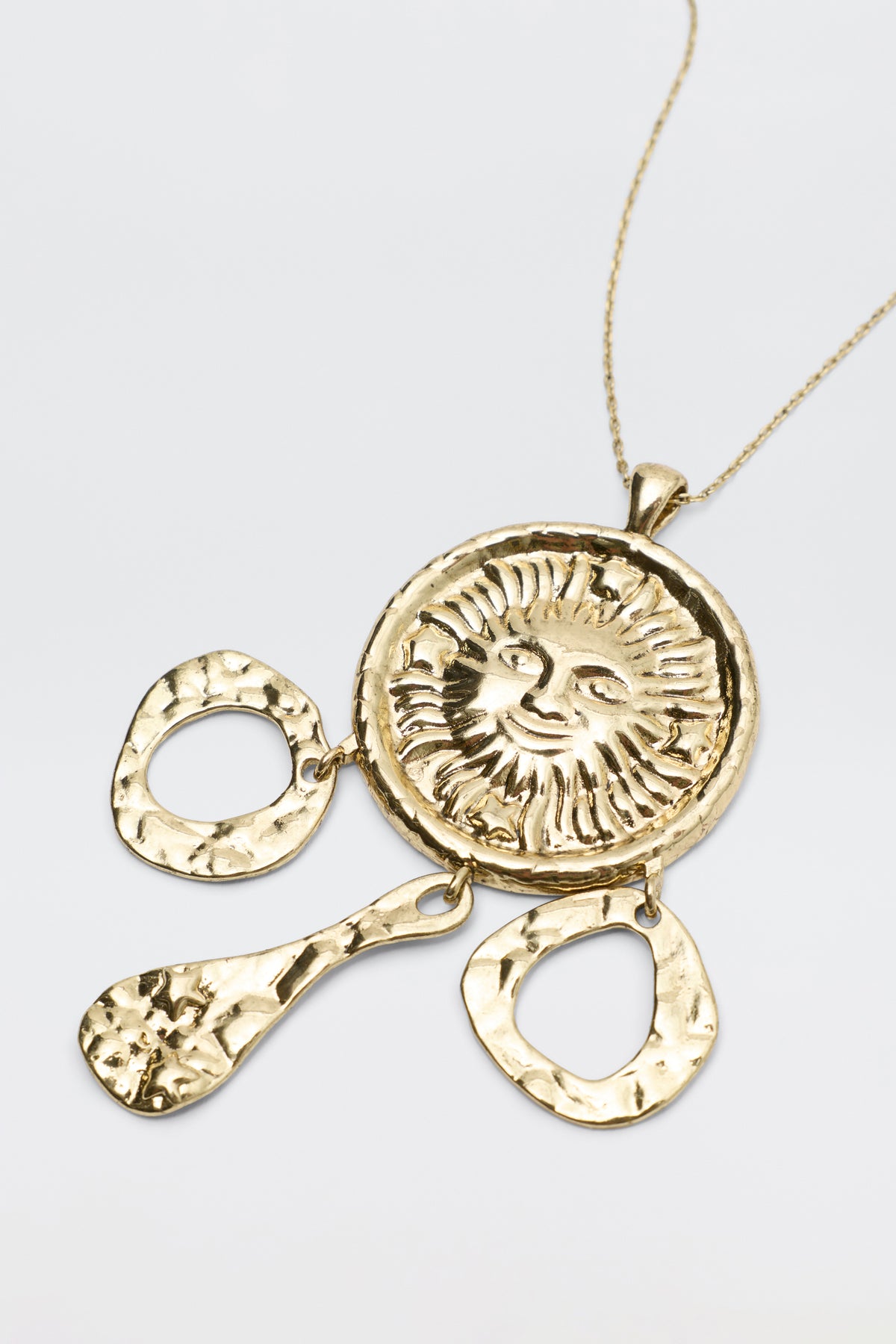 The Zahra - Gold necklace features a round sun face medallion pendant with three hammered gold dangles hanging below.