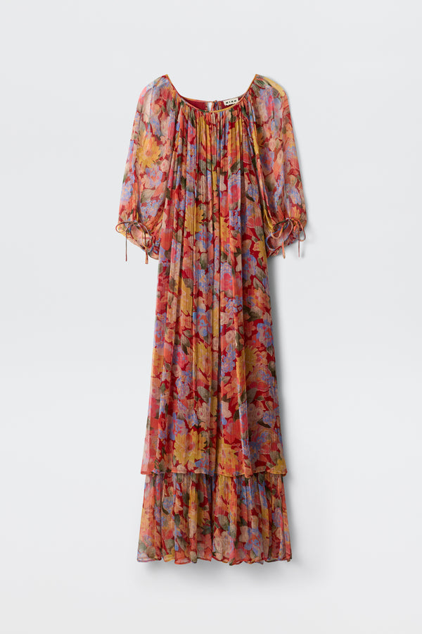 The Hayden - Chelsea Floral Red is a long, flowy dress adorned with a vibrant floral pattern in shades of red, orange, blue, and purple. It features puffed half sleeves and a ruffled hem and is displayed against a plain white background.