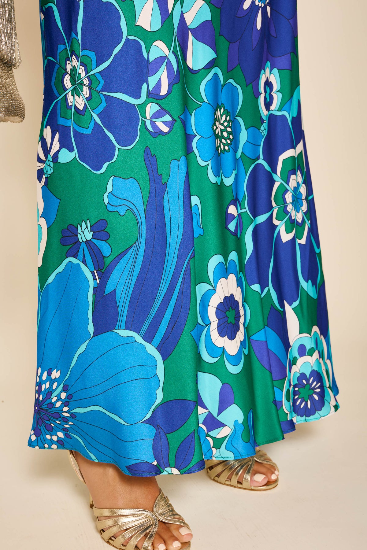 Wearing the marni - miami floral emerald skirt with bold blue and green patterns and godet panels, a person stands on a light floor, showing only their legs and feet in strappy metallic sandals.